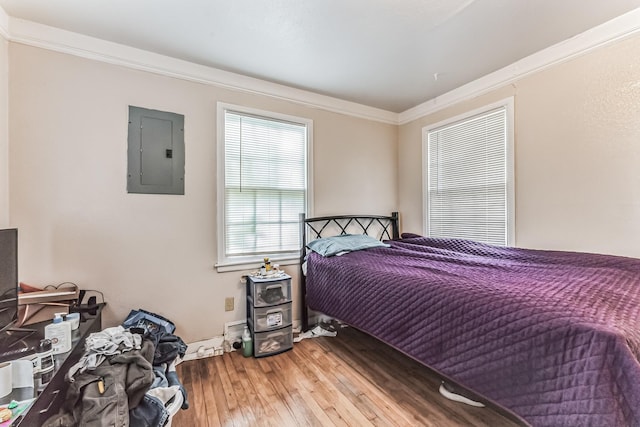 bedroom with electric panel, hardwood / wood-style floors, and ornamental molding
