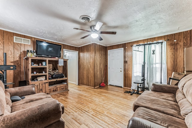 living room featuring hardwood / wood-style floors, ceiling fan, wooden walls, and a textured ceiling