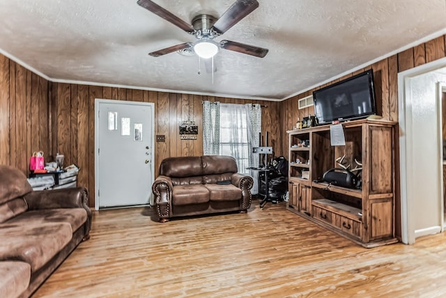 living area featuring light wood-style floors, ceiling fan, wooden walls, and a textured ceiling
