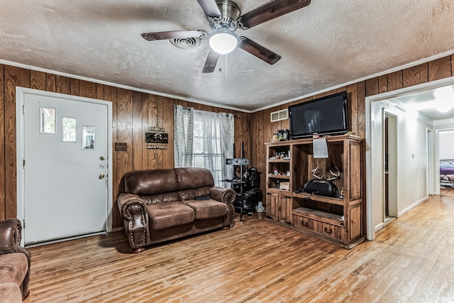 living room featuring light hardwood / wood-style floors, a textured ceiling, ceiling fan, and wooden walls