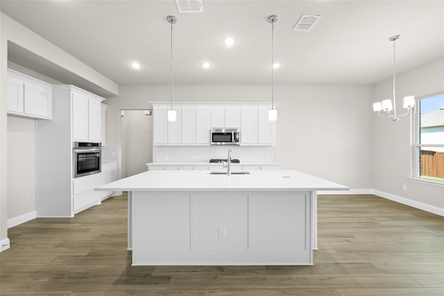 kitchen featuring white cabinets, stainless steel appliances, decorative light fixtures, a center island with sink, and sink