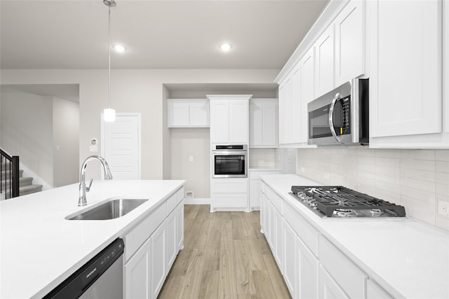 kitchen featuring pendant lighting, light hardwood / wood-style floors, sink, white cabinetry, and stainless steel appliances