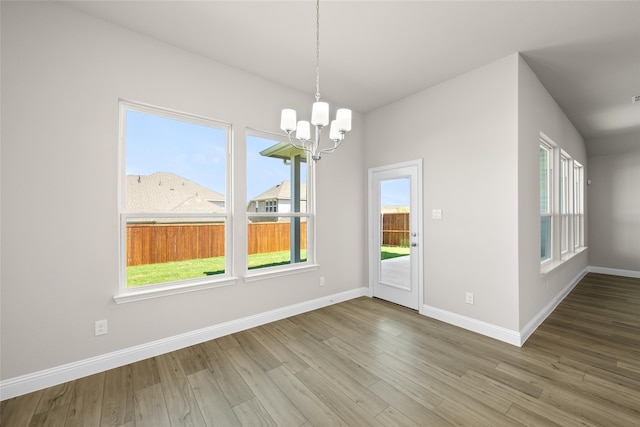 unfurnished dining area with a notable chandelier, a wealth of natural light, and wood-type flooring