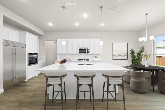 kitchen featuring white cabinetry, appliances with stainless steel finishes, hanging light fixtures, and a kitchen island with sink