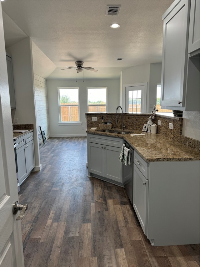 kitchen with kitchen peninsula, ceiling fan, stainless steel dishwasher, dark hardwood / wood-style floors, and sink