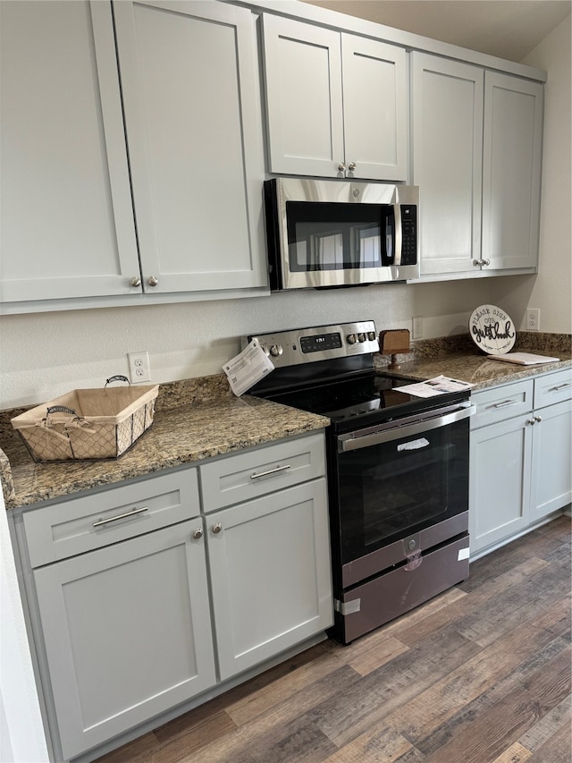 kitchen featuring dark wood-type flooring, dark stone counters, and stainless steel appliances