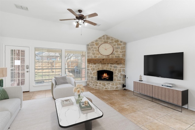 tiled living room with ceiling fan, vaulted ceiling, and a stone fireplace