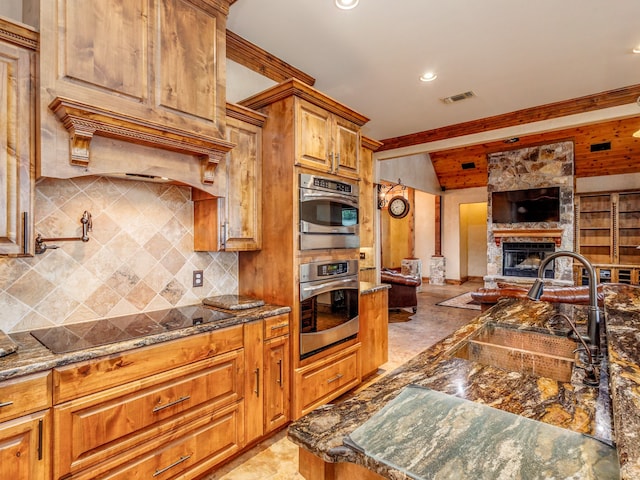 kitchen with black electric stovetop, tasteful backsplash, a fireplace, light tile patterned floors, and dark stone counters