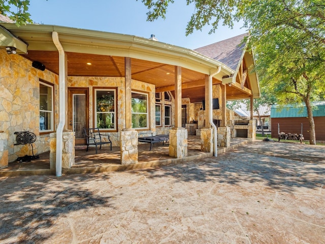 exterior space featuring stone siding, a shingled roof, an outdoor structure, and an exterior structure