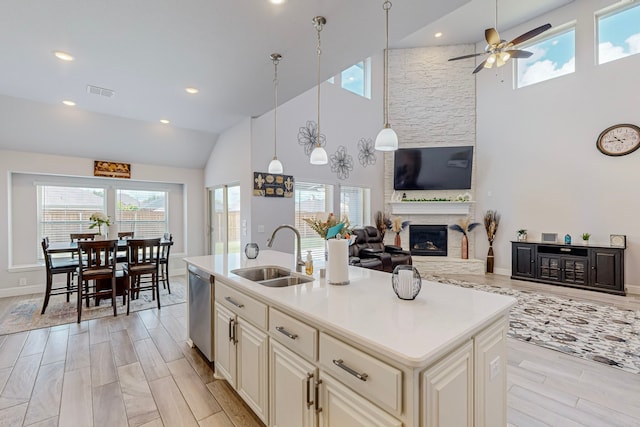 kitchen with a large fireplace, stainless steel dishwasher, ceiling fan, an island with sink, and sink