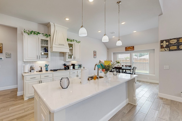 kitchen featuring lofted ceiling, custom exhaust hood, decorative backsplash, pendant lighting, and a center island with sink