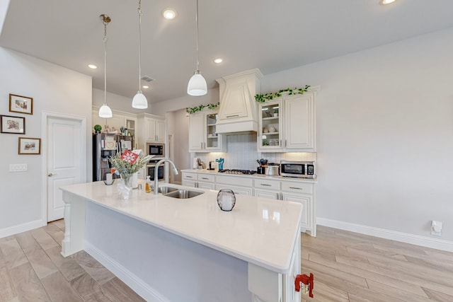 kitchen with appliances with stainless steel finishes, sink, backsplash, custom exhaust hood, and a large island with sink