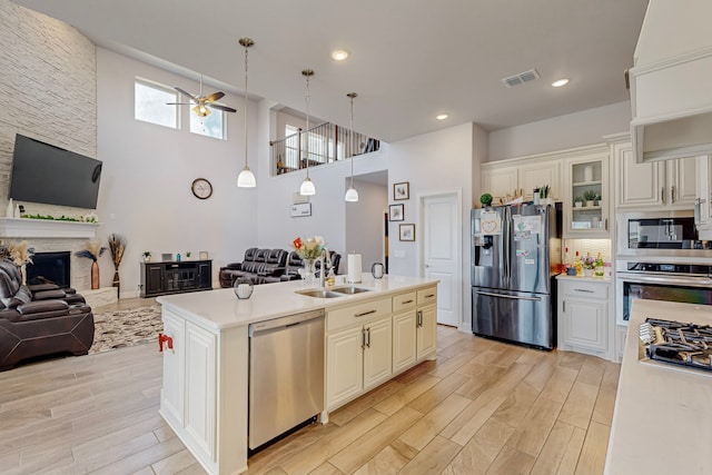 kitchen featuring a kitchen island with sink, ceiling fan, light hardwood / wood-style floors, appliances with stainless steel finishes, and a fireplace