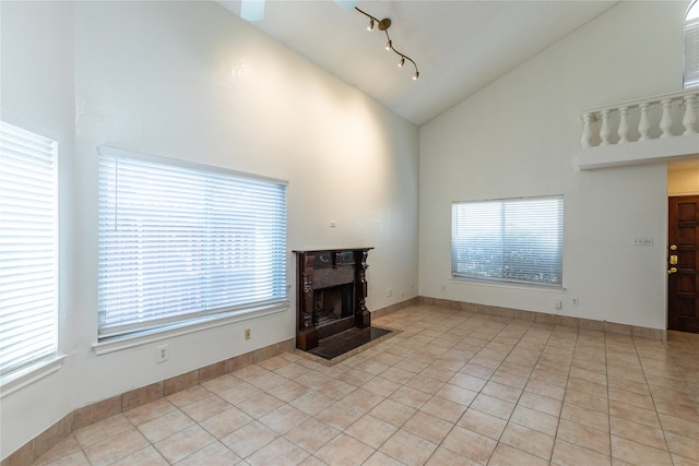 unfurnished living room featuring high vaulted ceiling, rail lighting, a healthy amount of sunlight, and light tile patterned floors