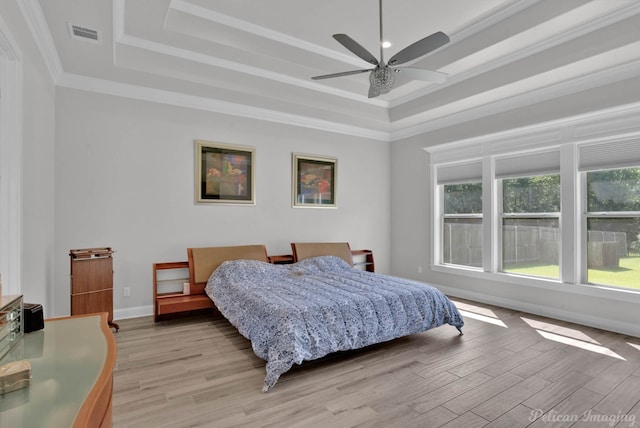 bedroom with ceiling fan, multiple windows, a tray ceiling, and light wood-type flooring