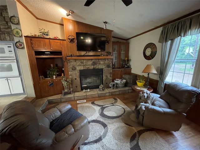 living room with hardwood / wood-style flooring, ceiling fan, ornamental molding, vaulted ceiling, and a stone fireplace