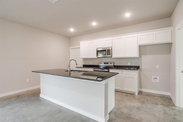 kitchen featuring appliances with stainless steel finishes, white cabinetry, dark stone counters, sink, and a center island with sink