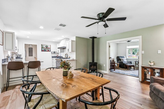 dining space featuring a wood stove, light hardwood / wood-style floors, sink, and ceiling fan