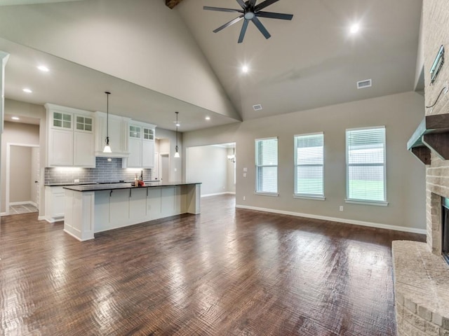 kitchen featuring a fireplace, decorative light fixtures, tasteful backsplash, white cabinets, and a kitchen island with sink