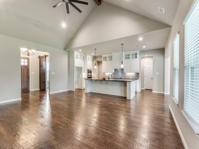 unfurnished living room with sink, high vaulted ceiling, beamed ceiling, a barn door, and ceiling fan with notable chandelier