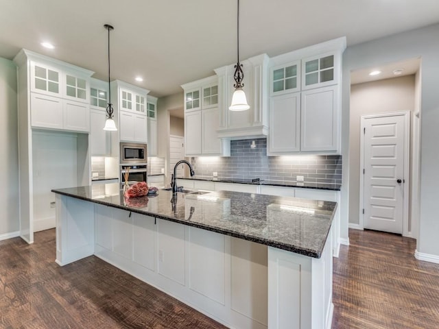 kitchen with appliances with stainless steel finishes, sink, a kitchen island with sink, and dark stone counters