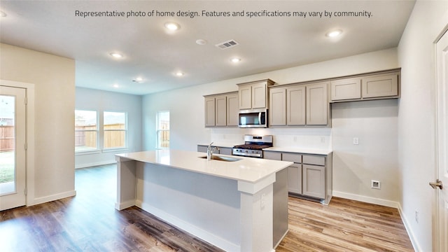 kitchen featuring an island with sink, gray cabinetry, sink, appliances with stainless steel finishes, and light hardwood / wood-style floors