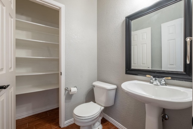 bathroom with a textured wall, toilet, baseboards, and wood finished floors