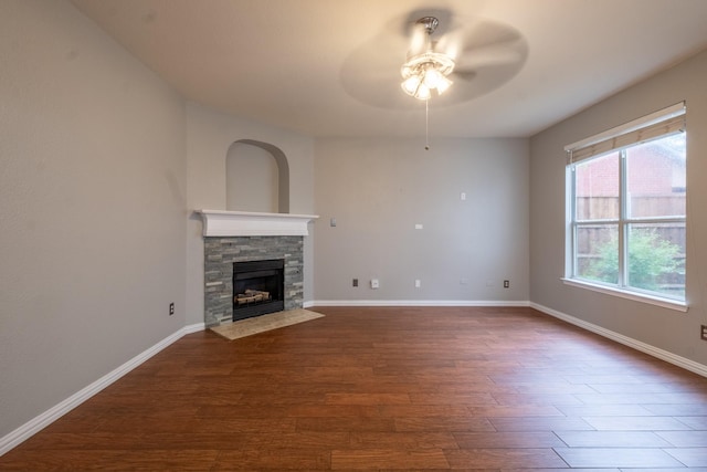 unfurnished living room with dark wood-style floors, ceiling fan, baseboards, and a stone fireplace