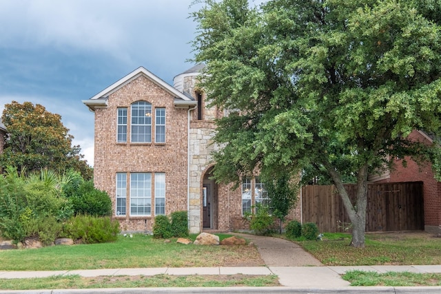 traditional home with a front yard, stone siding, brick siding, and fence