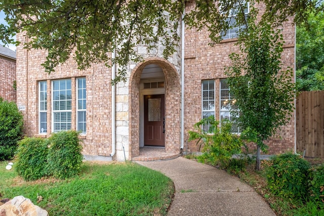 view of exterior entry featuring brick siding and fence