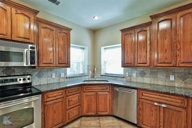 kitchen with light tile patterned floors, stainless steel appliances, tasteful backsplash, dark stone counters, and sink