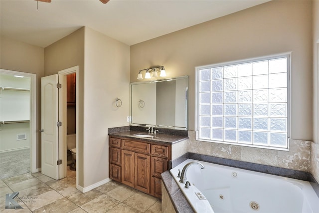 bathroom featuring toilet, a wealth of natural light, tiled tub, and vanity