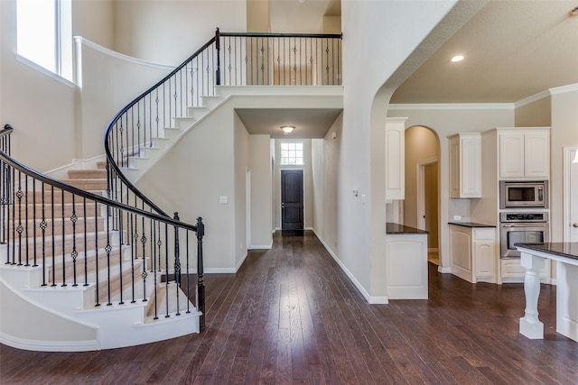 entryway with dark wood-type flooring, a towering ceiling, and ornamental molding