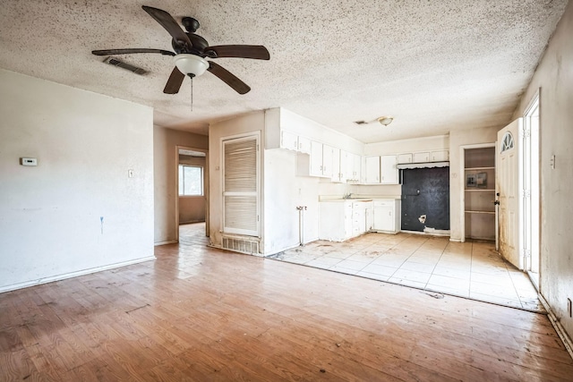 unfurnished living room with sink, a textured ceiling, ceiling fan, and light hardwood / wood-style floors