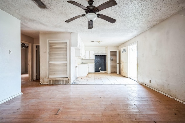 unfurnished living room featuring a textured ceiling, ceiling fan, and light hardwood / wood-style flooring