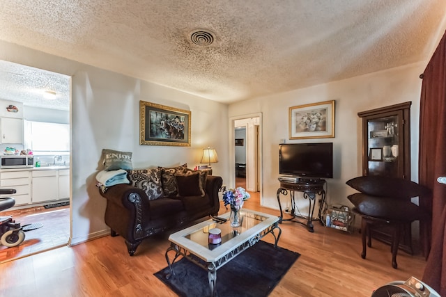 living room with sink, a textured ceiling, and light hardwood / wood-style flooring