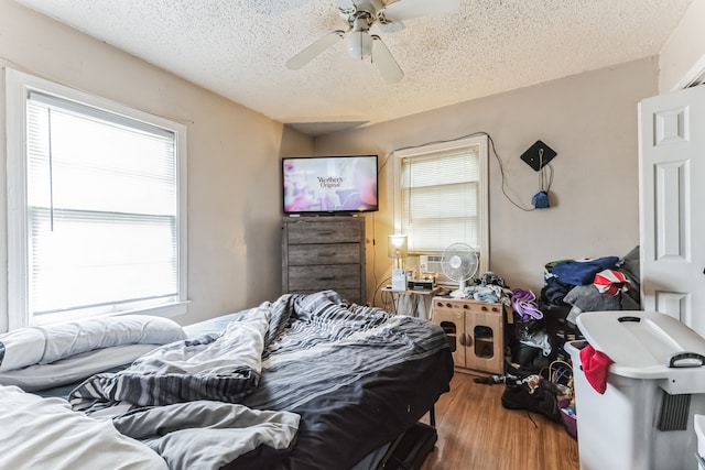 bedroom featuring ceiling fan, multiple windows, a textured ceiling, and hardwood / wood-style flooring