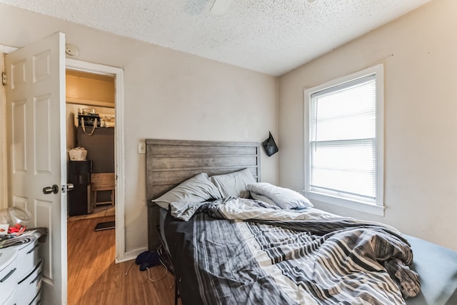 bedroom with a closet, a textured ceiling, hardwood / wood-style flooring, and a spacious closet