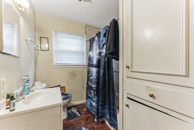 bathroom featuring wood-type flooring, toilet, vanity, and a textured ceiling