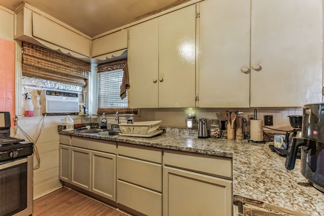 kitchen with cream cabinetry, range with gas stovetop, light stone countertops, wood-type flooring, and sink