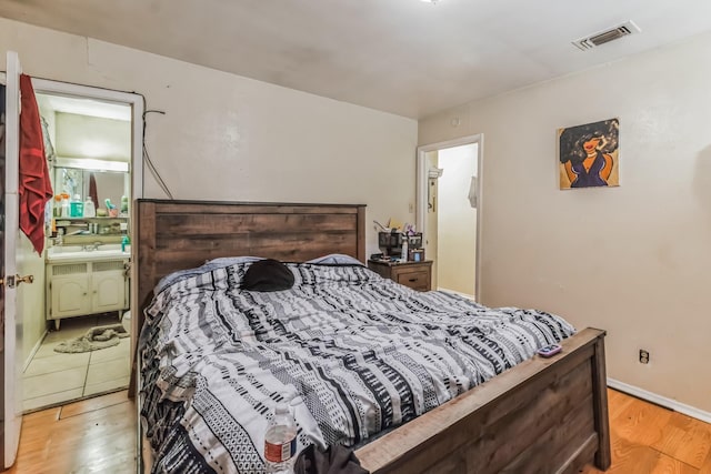 bedroom featuring light wood-style floors, visible vents, and connected bathroom