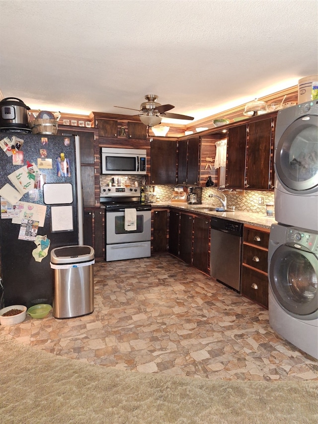 kitchen with dark brown cabinetry, stacked washer and clothes dryer, ceiling fan, stainless steel appliances, and decorative backsplash