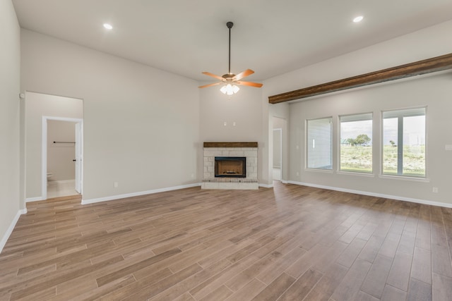 unfurnished living room featuring light wood-type flooring, ceiling fan, and a stone fireplace