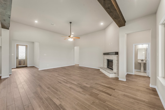 unfurnished living room with ceiling fan, beamed ceiling, sink, a fireplace, and light wood-type flooring