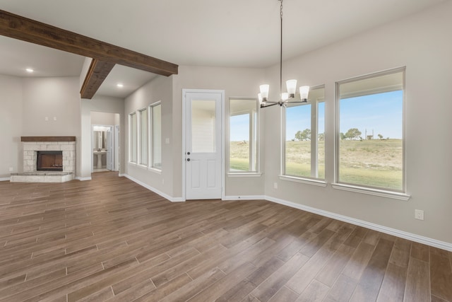 unfurnished living room with a notable chandelier, beam ceiling, a fireplace, and dark hardwood / wood-style flooring