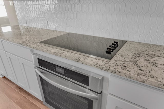 interior details featuring light stone counters, black electric cooktop, white cabinets, and stainless steel oven