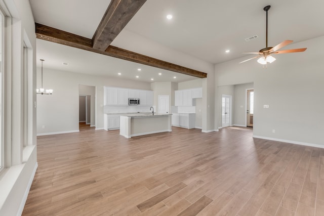 unfurnished living room featuring ceiling fan with notable chandelier, light hardwood / wood-style floors, beam ceiling, and sink