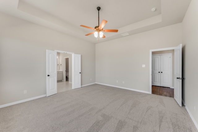 unfurnished bedroom featuring a tray ceiling, ceiling fan, and light colored carpet