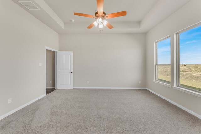 unfurnished room with a healthy amount of sunlight, carpet flooring, a tray ceiling, and ceiling fan