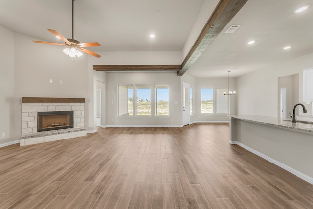 unfurnished living room with sink, beam ceiling, hardwood / wood-style flooring, a fireplace, and ceiling fan with notable chandelier